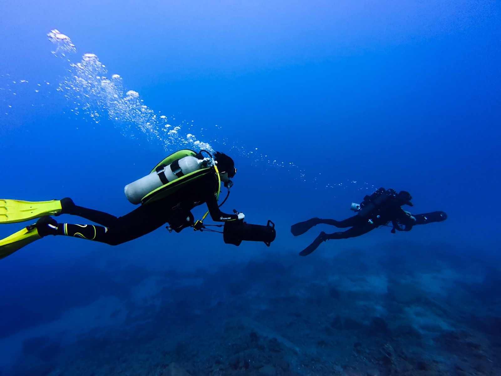 Two divers on scooters gliding over the reef in deep blue water