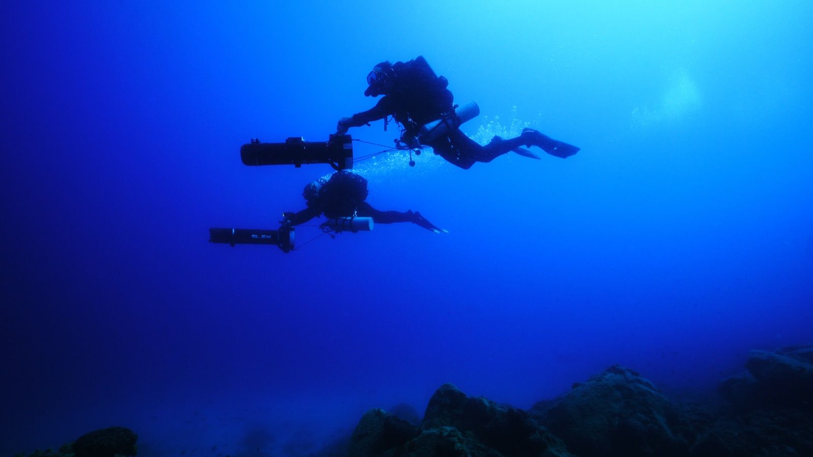 Two divers on scooters silhouetted in deep blue