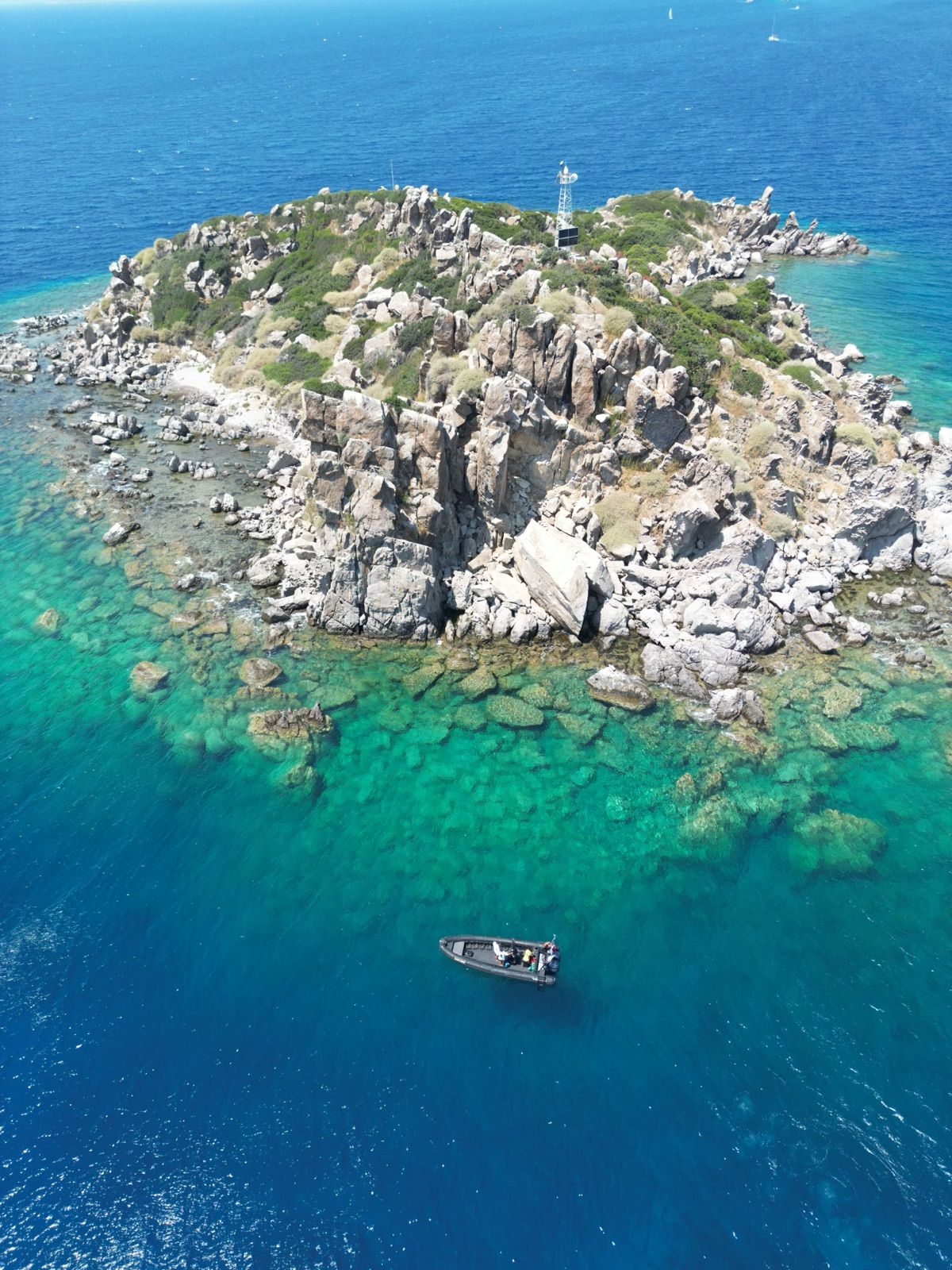 A rocky islet ringed by clear shallow water, the RIB anchored off the point
