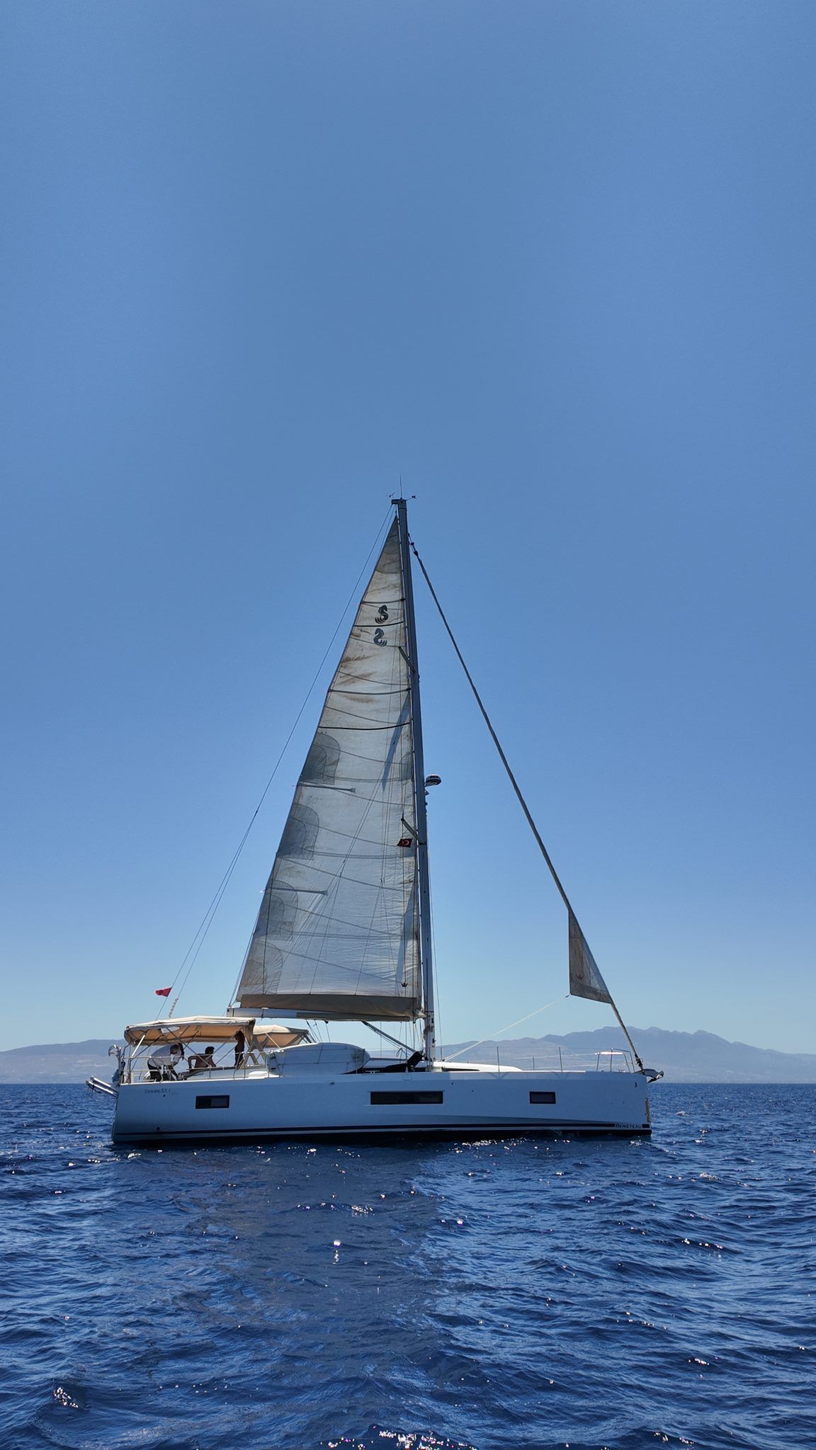 The yacht under full sail offshore, crew visible in the cockpit