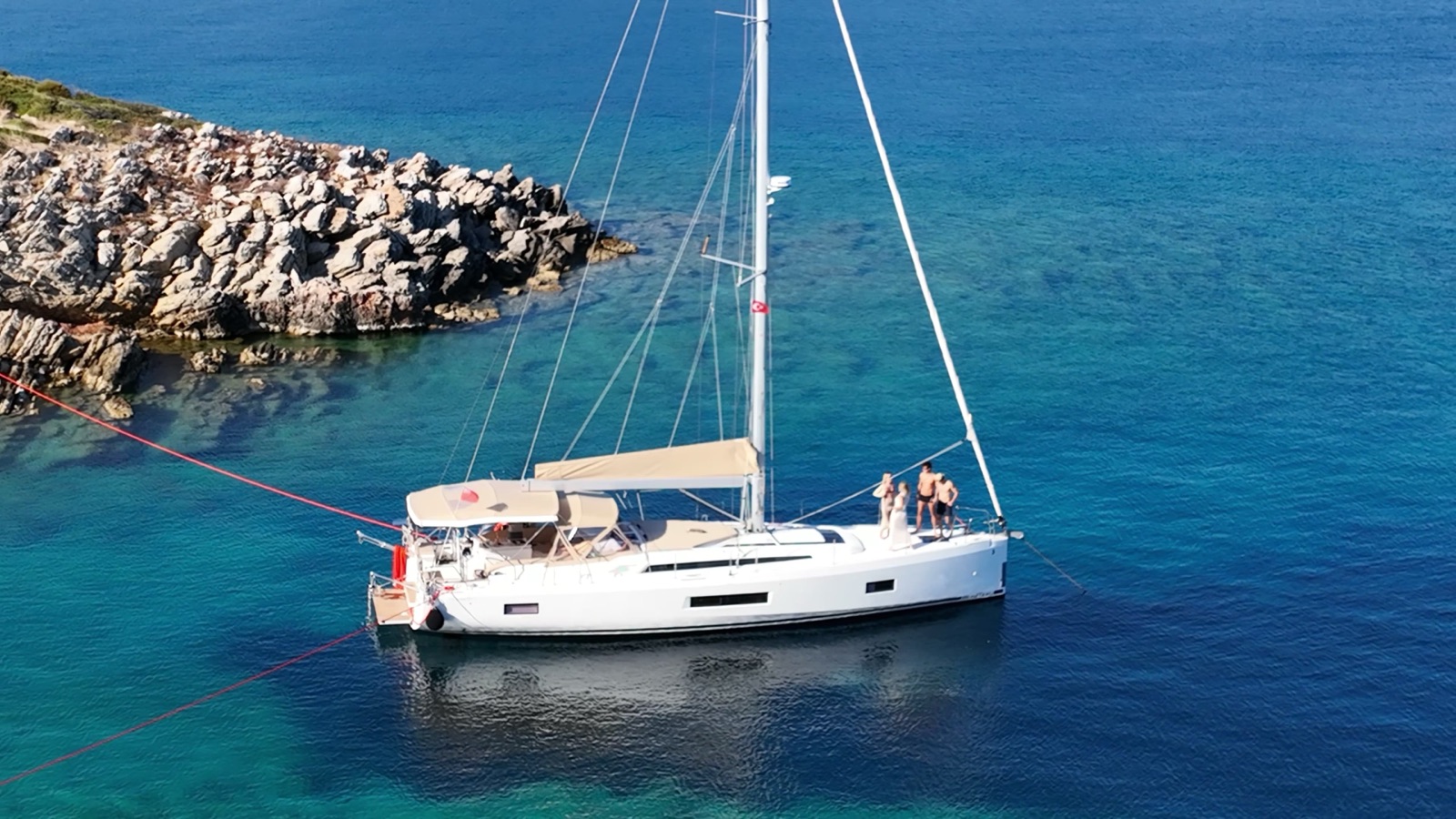 The Oceanis anchored close in against a rocky shore in clear turquoise water