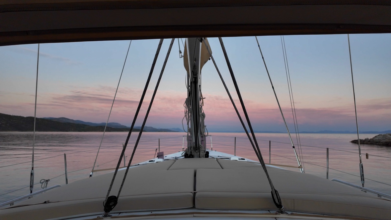 Dawn over the Oceanis 51.1 bow at anchor, still water and a pink sky