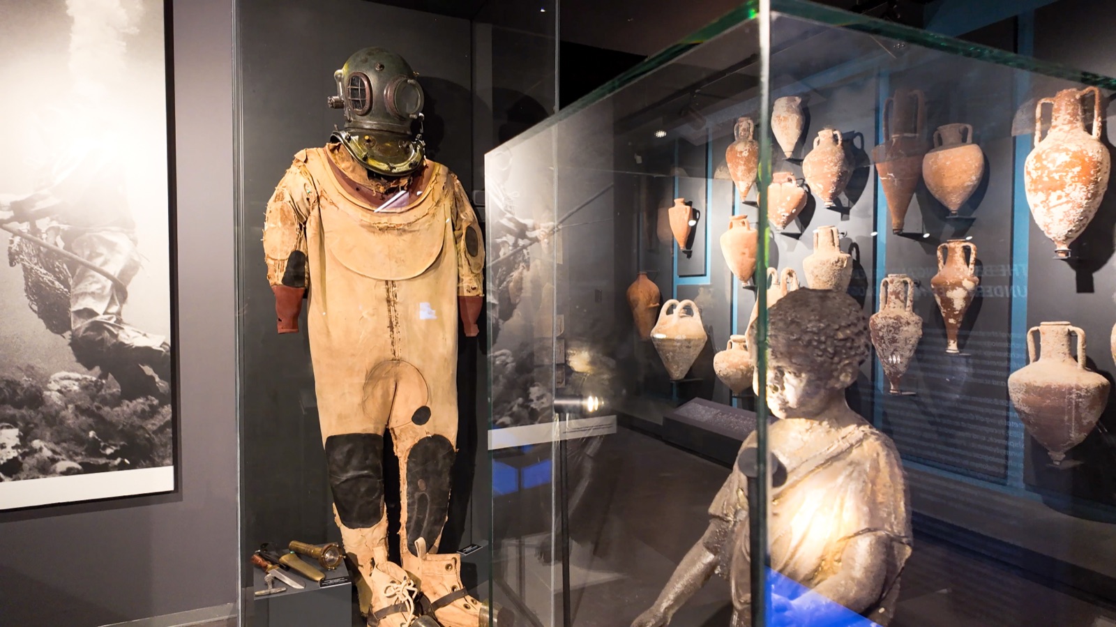 Early hard-hat diving suit beside amphora wall